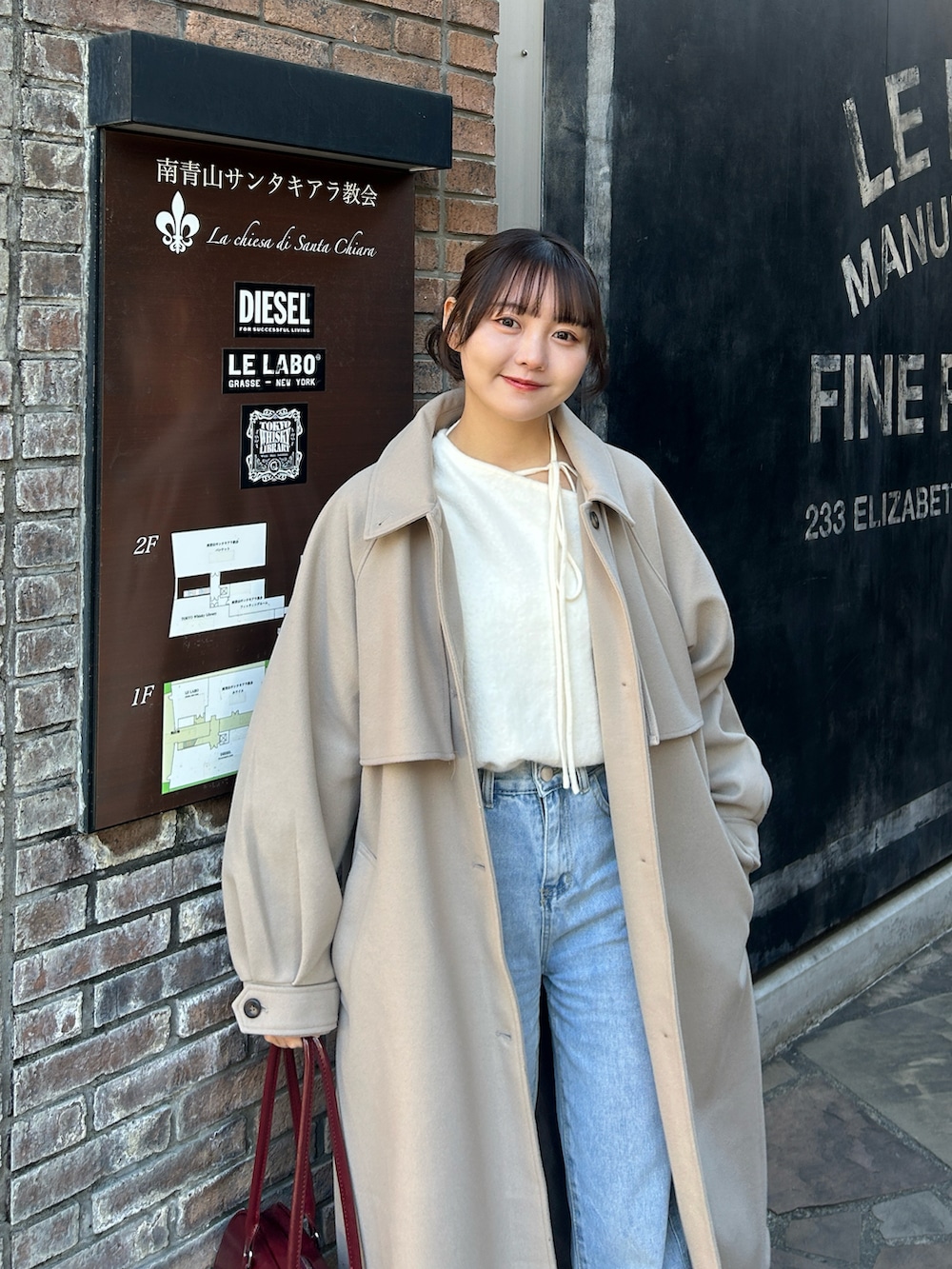 ホワイト系のニット/セーター、ベージュ系のステンカラーコート、ブルー系のデニムパンツを着用したレディースの冬コーディネートの2枚目の写真