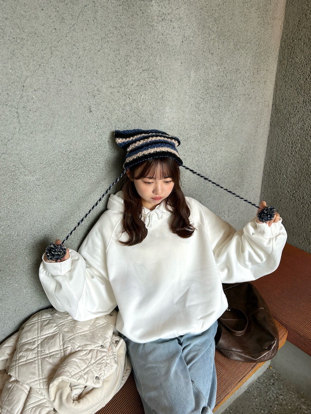 ホワイト系のパーカー、ブラウン系のショルダーバッグ、ブルー系のデニムパンツを着用したレディースの秋コーディネートの2枚目の写真