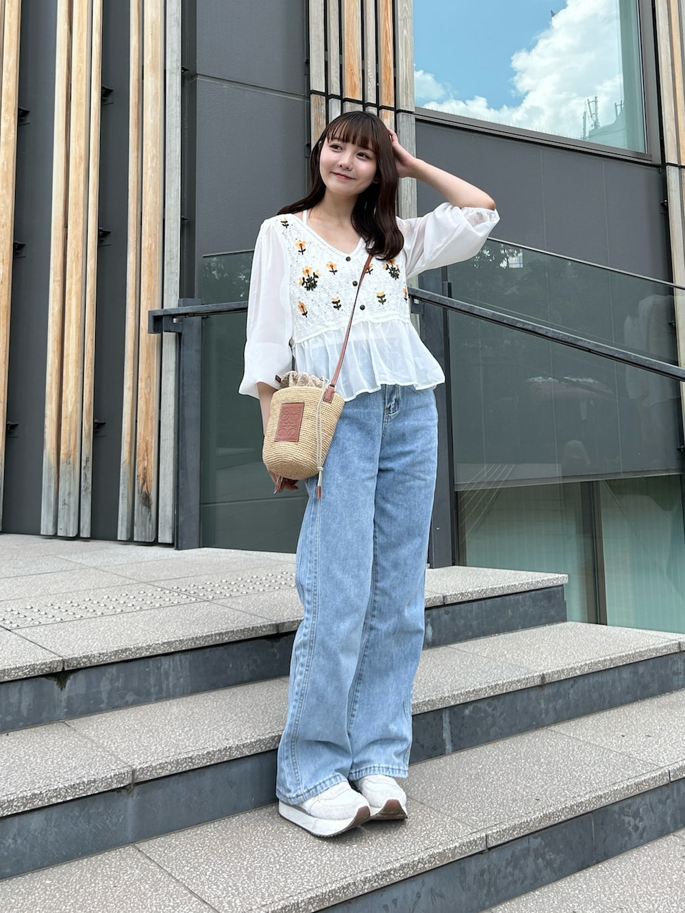 ブルー系のデニムパンツ、グレー系のスニーカー、ベージュ系のかごバッグを着用したレディースの夏コーディネートの2枚目の写真