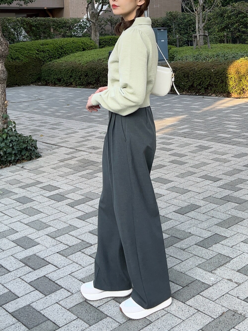 グリーン系のニット/セーター、ホワイト系のハンドバッグ、グレー系のパンツを着用したレディースの春コーディネートの5枚目の写真