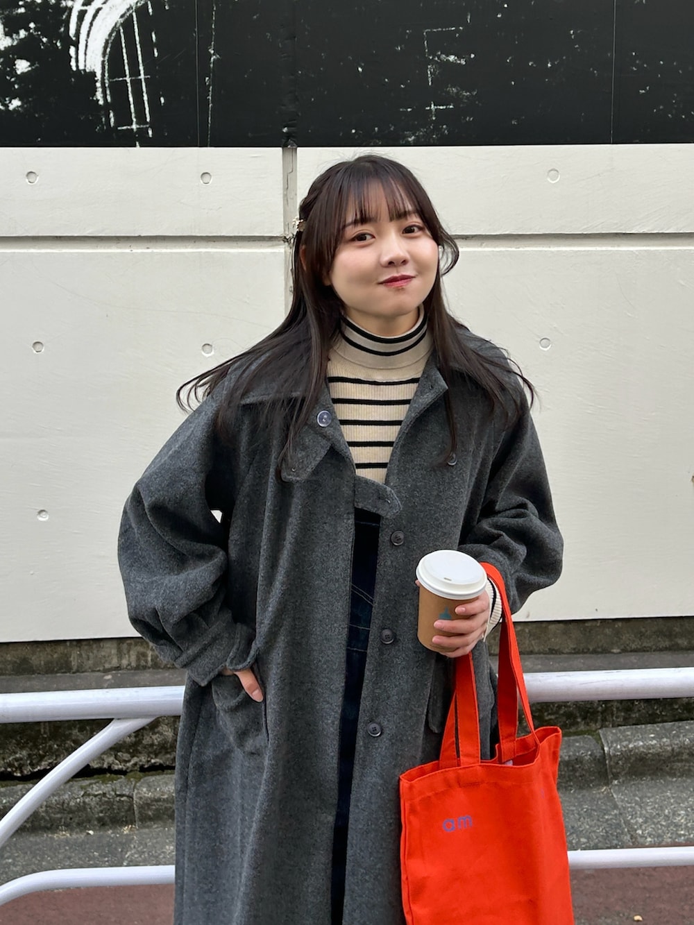 ブラック系のステンカラーコート、ホワイト系のニット/セーター、ブルー系のサロペット/オーバーオールを着用したレディースの冬コーディネートの2枚目の写真