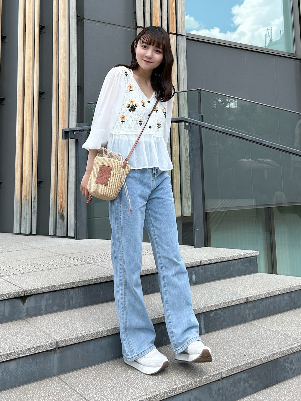 ブルー系のデニムパンツ、グレー系のスニーカー、ベージュ系のかごバッグを着用したレディースの夏コーディネートの3枚目の写真