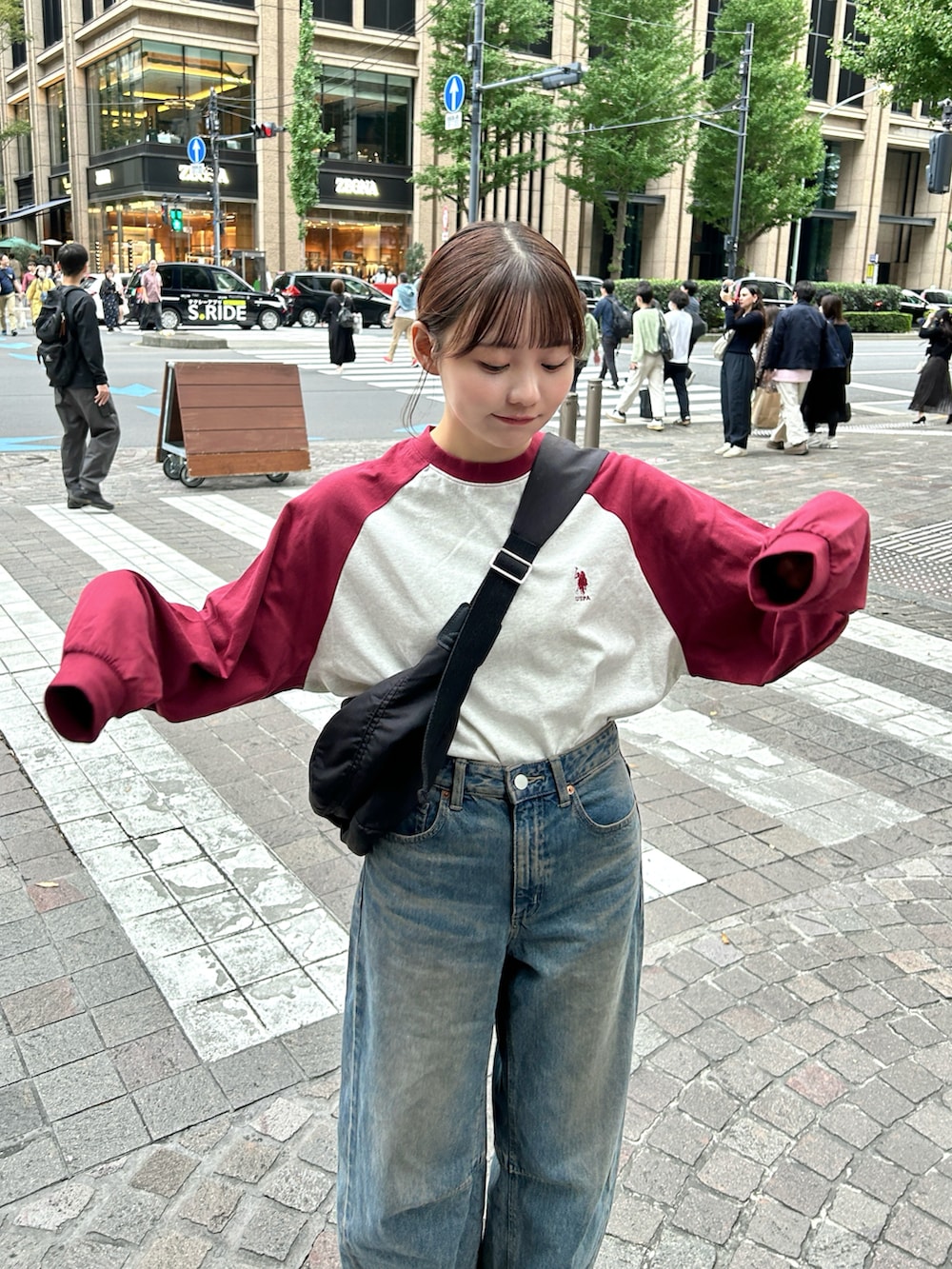 レッド系のTシャツ/カットソー、ブラック系のショルダーバッグ、ブルー系のデニムパンツを着用したレディースの秋コーディネートの3枚目の写真