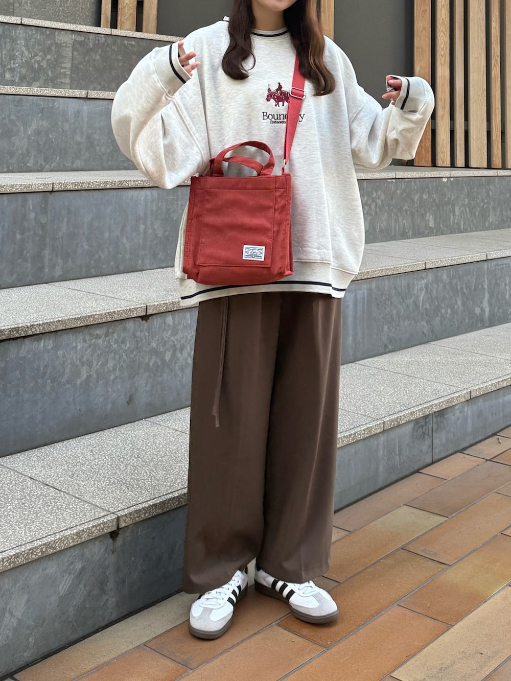 レッド系のショルダーバッグ、ベージュ系のスウェット、ブラウン系のその他パンツを着用したレディースの冬コーディネートの2枚目の写真