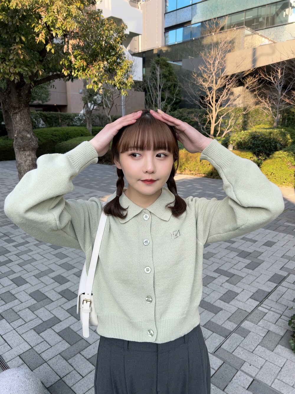 グリーン系のニット/セーター、ホワイト系のハンドバッグ、グレー系のパンツを着用したレディースの春コーディネートの3枚目の写真