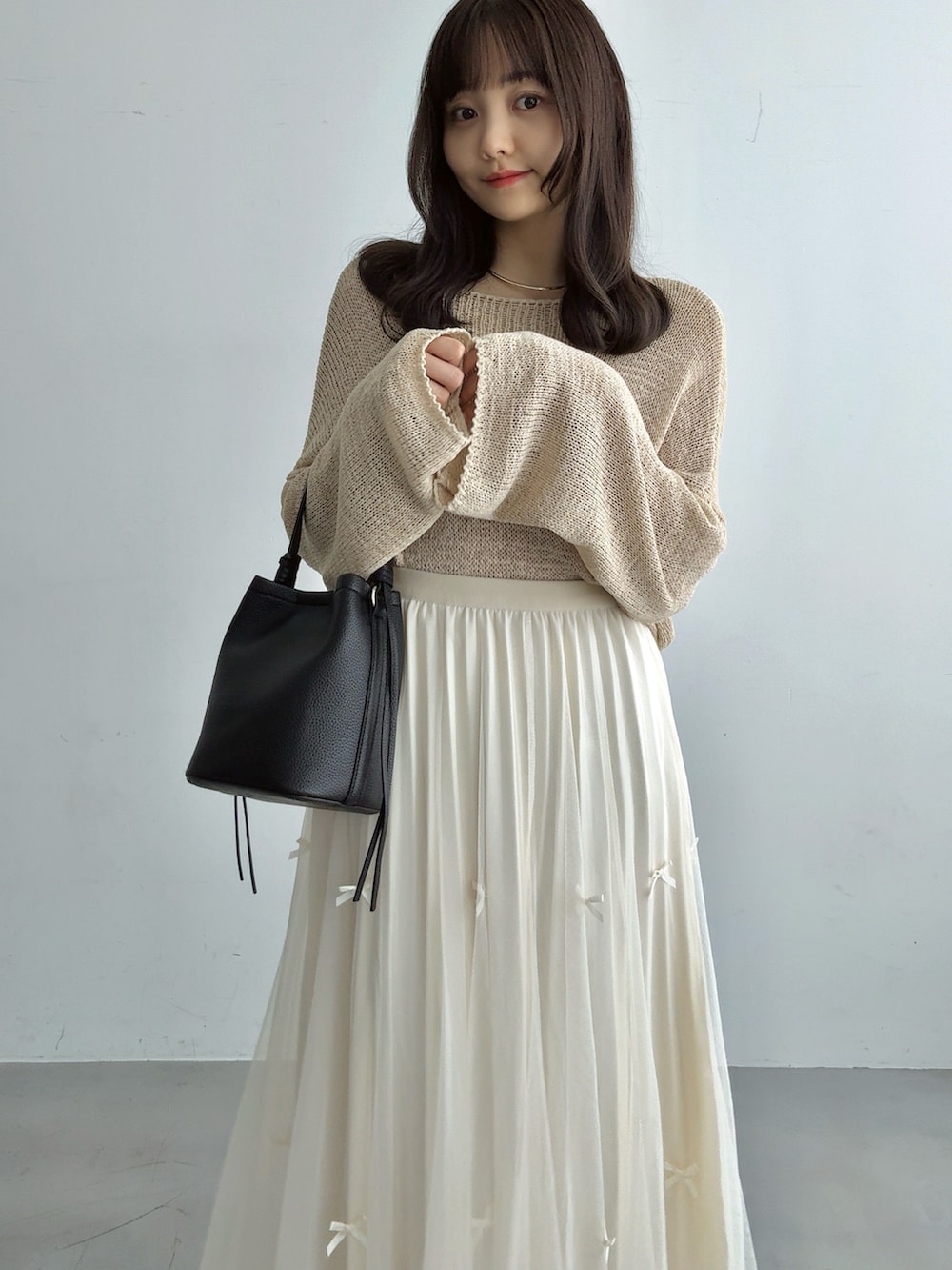 ベージュ系のニット/セーター、ホワイト系のスカート、ブラック系のハンドバッグを着用したレディースの秋コーディネートの4枚目の写真