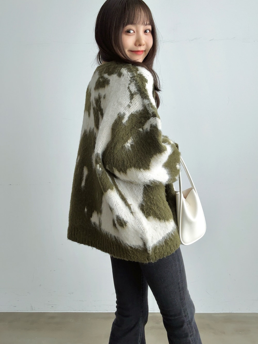 グリーン系のニット/セーター、ブラック系のデニムパンツ、ホワイト系のハンドバッグを着用したレディースの冬コーディネートの4枚目の写真