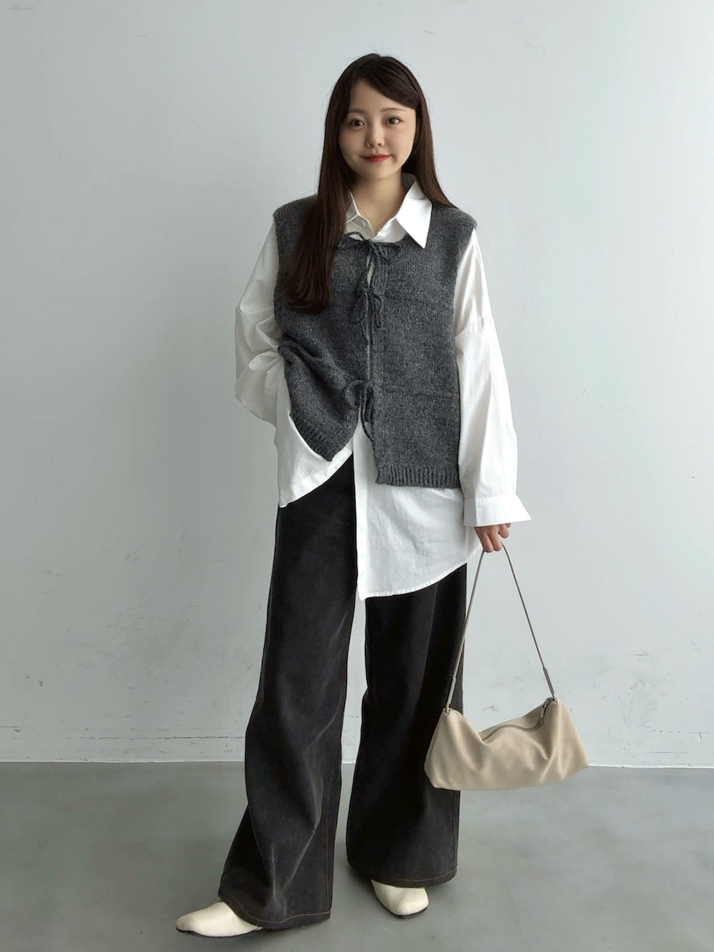 グレー系のベスト、ブラック系のその他パンツ、ホワイト系のショルダーバッグを着用したレディースの秋コーディネートの2枚目の写真