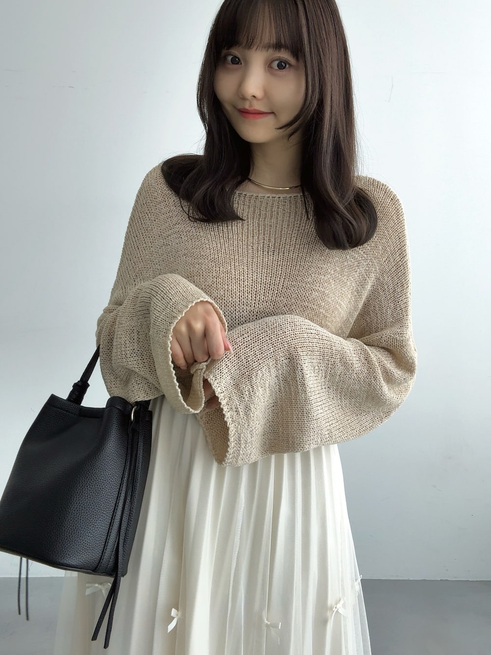 ベージュ系のニット/セーター、ホワイト系のスカート、ブラック系のハンドバッグを着用したレディースの秋コーディネートの5枚目の写真