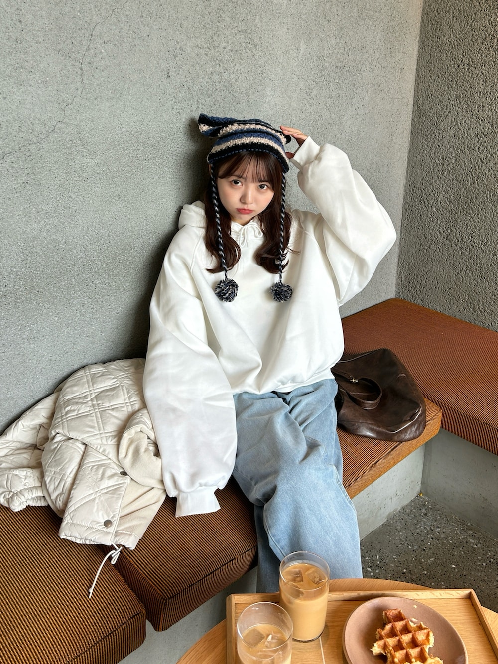 ホワイト系のパーカー、ブラウン系のショルダーバッグ、ブルー系のデニムパンツを着用したレディースの秋コーディネートの3枚目の写真