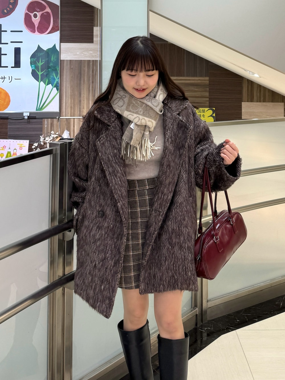 ブラウン系のスカート、レッド系のボストンバッグ、ブラウン系のピーコートを着用したレディースの冬コーディネートの2枚目の写真