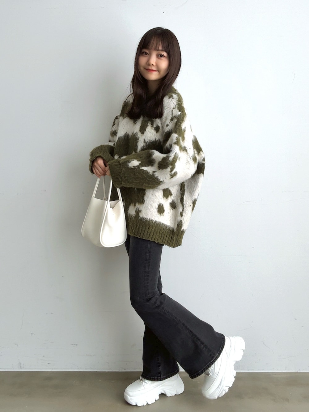 グリーン系のニット/セーター、ブラック系のデニムパンツ、ホワイト系のハンドバッグを着用したレディースの冬コーディネートの2枚目の写真