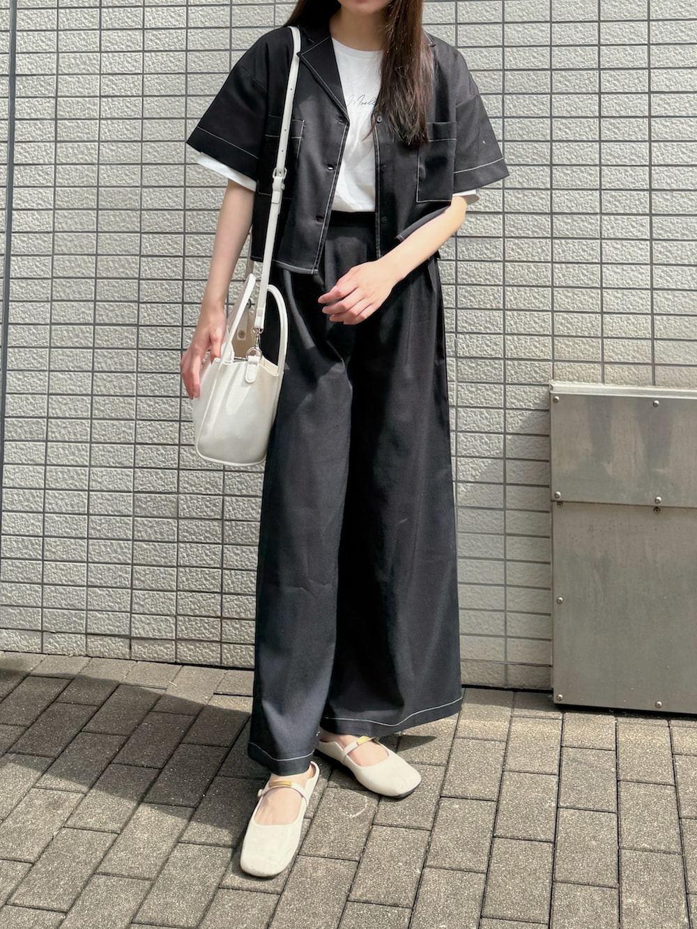 ブラック系のセットアップ、ホワイト系のハンドバッグ、ホワイト系のパンプスを着用したレディースの夏コーディネートの2枚目の写真
