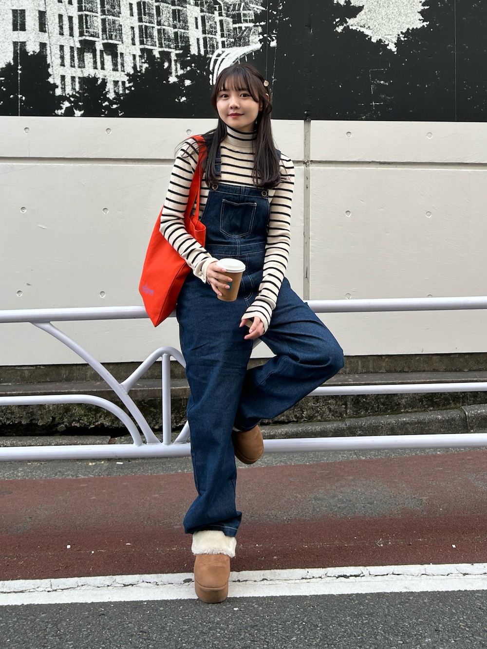 ブルー系のサロペット/オーバーオール、ホワイト系のニット/セーター、オレンジ系のトートバッグを着用したレディースの春コーディネートの2枚目の写真