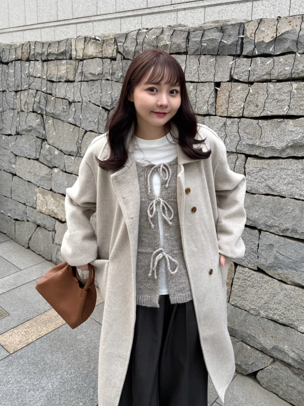 ベージュ系のステンカラーコート、ホワイト系のTシャツ/カットソー、ベージュ系のベストを着用したレディースの冬コーディネートの2枚目の写真