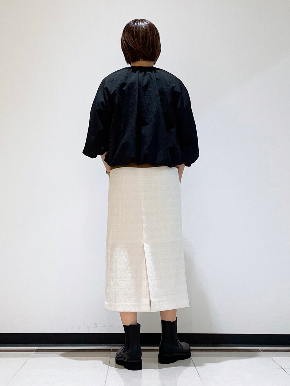 ブラック系のブーツ、ブラック系のショルダーバッグ、ホワイト系のスカートを着用したレディースの秋コーディネートの3枚目の写真