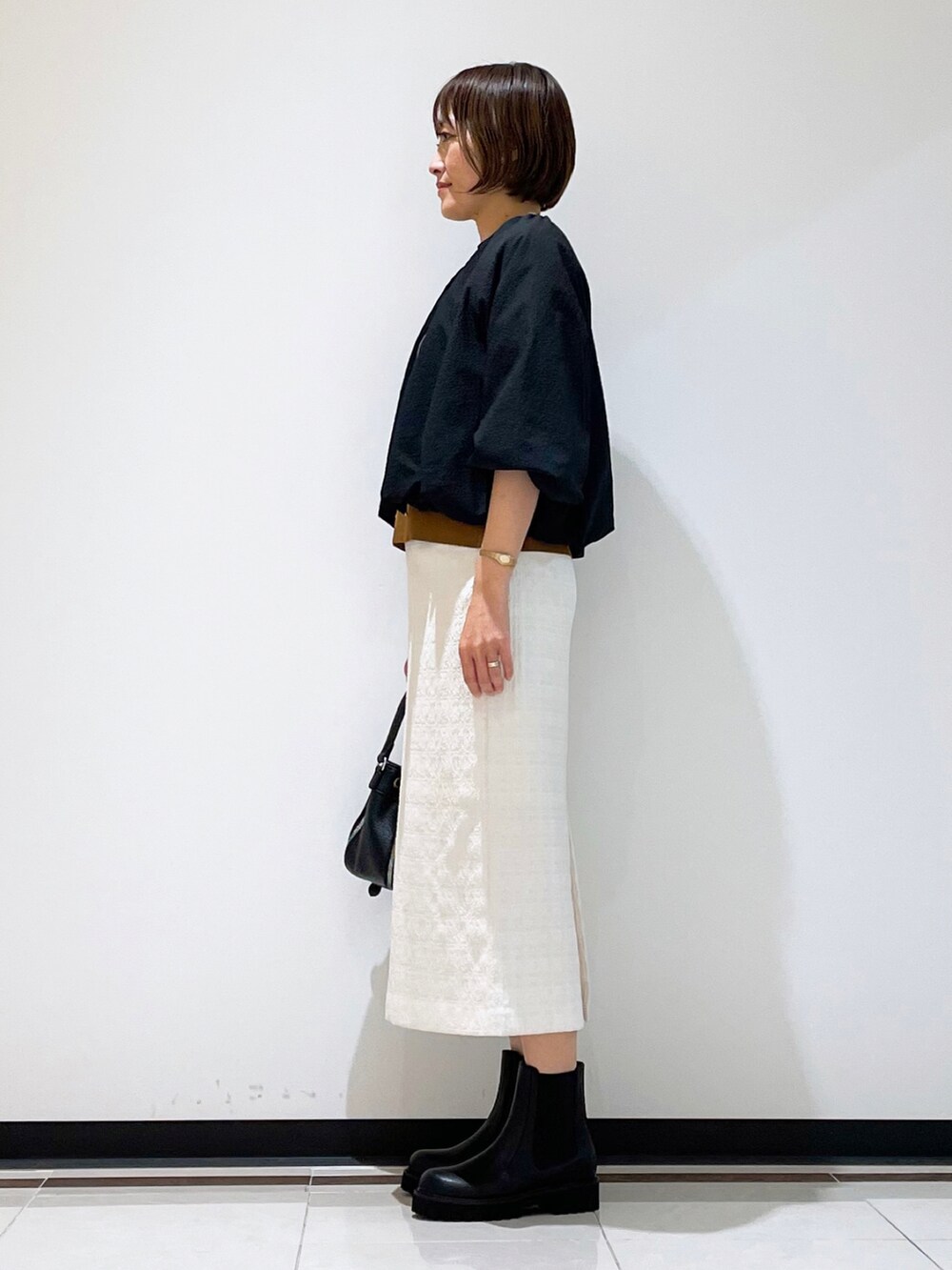 ブラック系のブーツ、ブラック系のショルダーバッグ、ホワイト系のスカートを着用したレディースの秋コーディネートの4枚目の写真