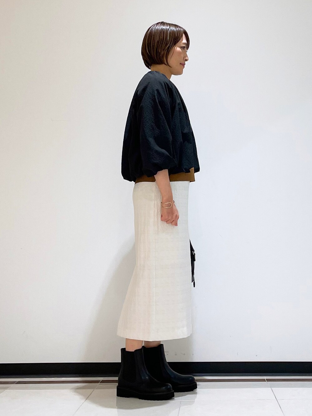 ブラック系のブーツ、ブラック系のショルダーバッグ、ホワイト系のスカートを着用したレディースの秋コーディネートの2枚目の写真