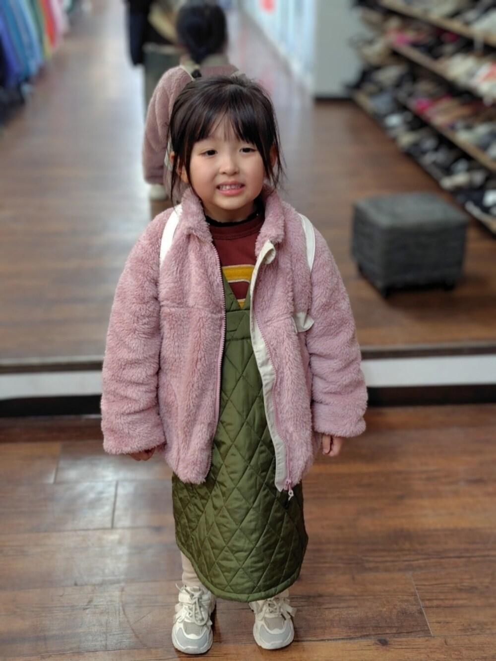 ピンク系のブルゾン、グリーン系のジャンパースカート、レッド系のスウェットを着用したキッズの冬コーディネートの3枚目の写真