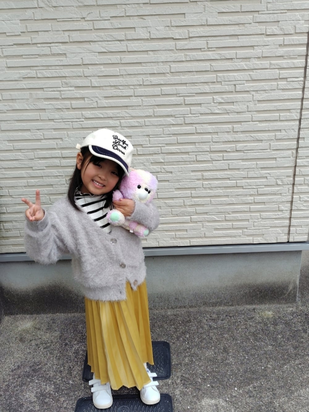 ベージュ系のカーディガン/ボレロ、ホワイト系のTシャツ/カットソー、イエロー系のスカートを着用したキッズの春コーディネートの2枚目の写真