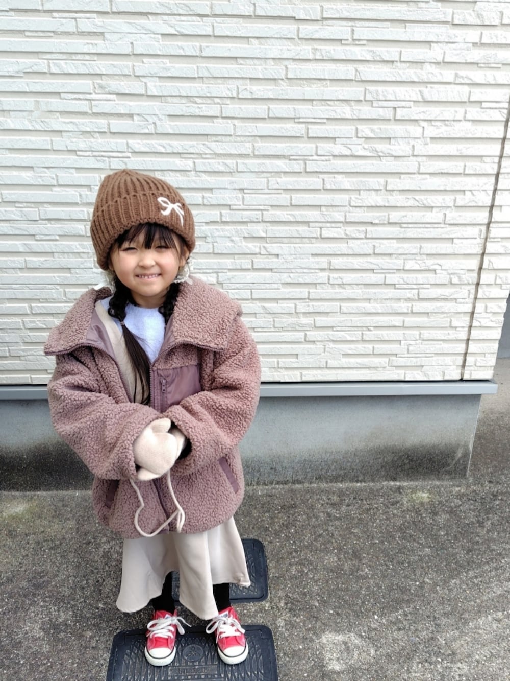ブラウン系のブルゾン、パープル系のニット/セーター、ベージュ系のジャンパースカートを着用したキッズの冬コーディネートの3枚目の写真