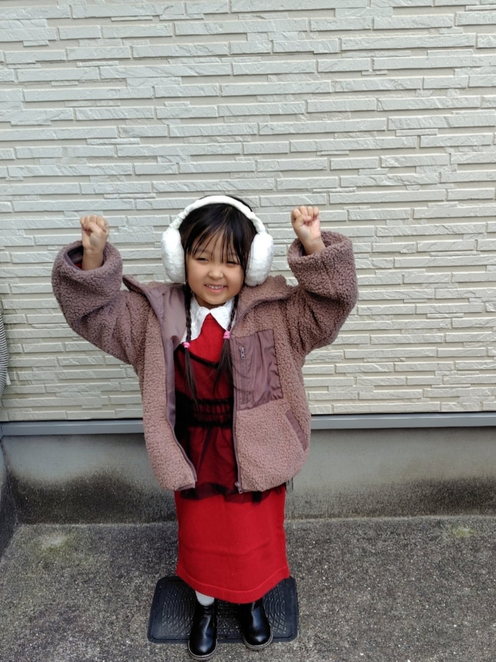 ブラウン系のブルゾン、レッド系のワンピース、ホワイト系のTシャツ/カットソーを着用したキッズの冬コーディネートの2枚目の写真