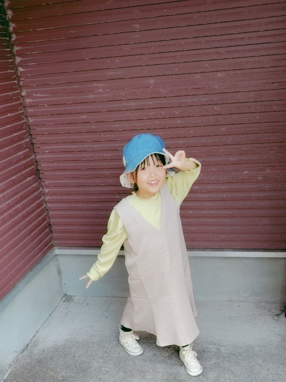 ベージュ系のジャンパースカート、グリーン系のTシャツ/カットソー、ホワイト系のスニーカーを着用したキッズの秋コーディネートの3枚目の写真