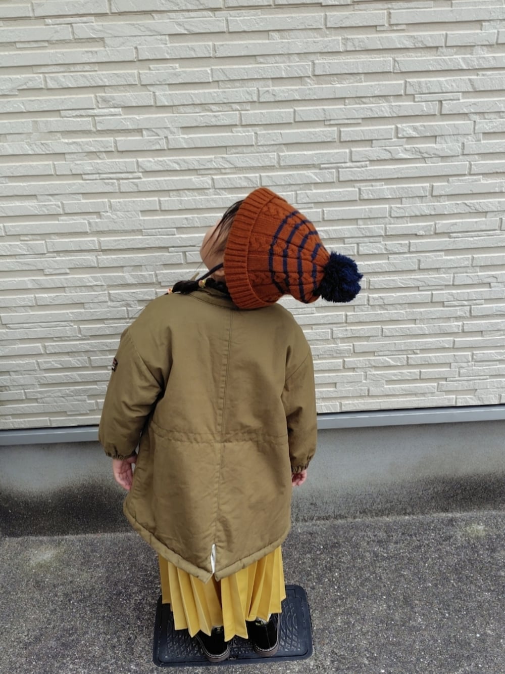 グリーン系のミリタリージャケット、グレー系のスウェット、イエロー系のスカートを着用したキッズの冬コーディネートの2枚目の写真