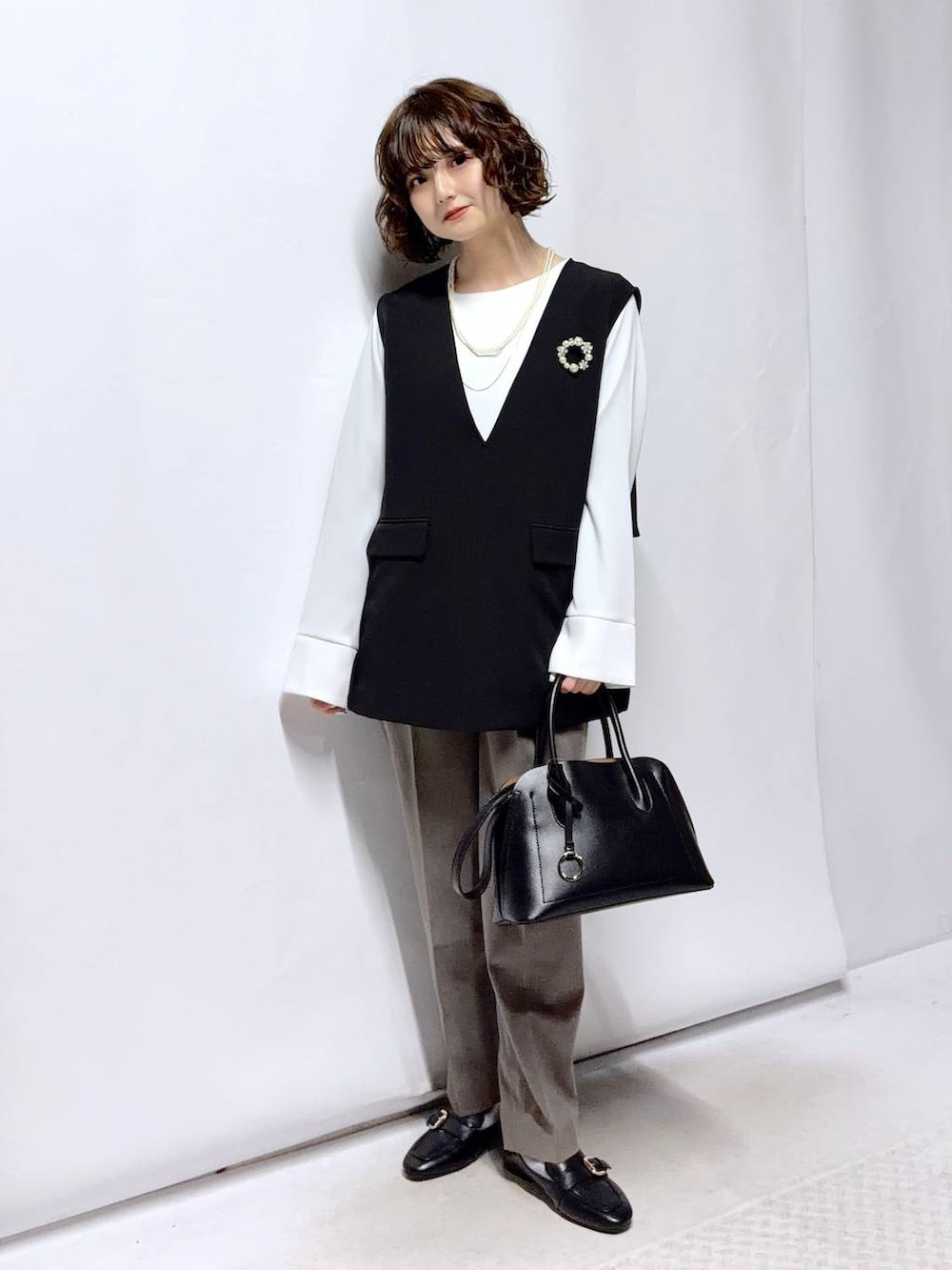 ブラック系のローファー、ブラック系のショルダーバッグ、ブラウン系のスラックスを着用したレディースの冬コーディネートの2枚目の写真