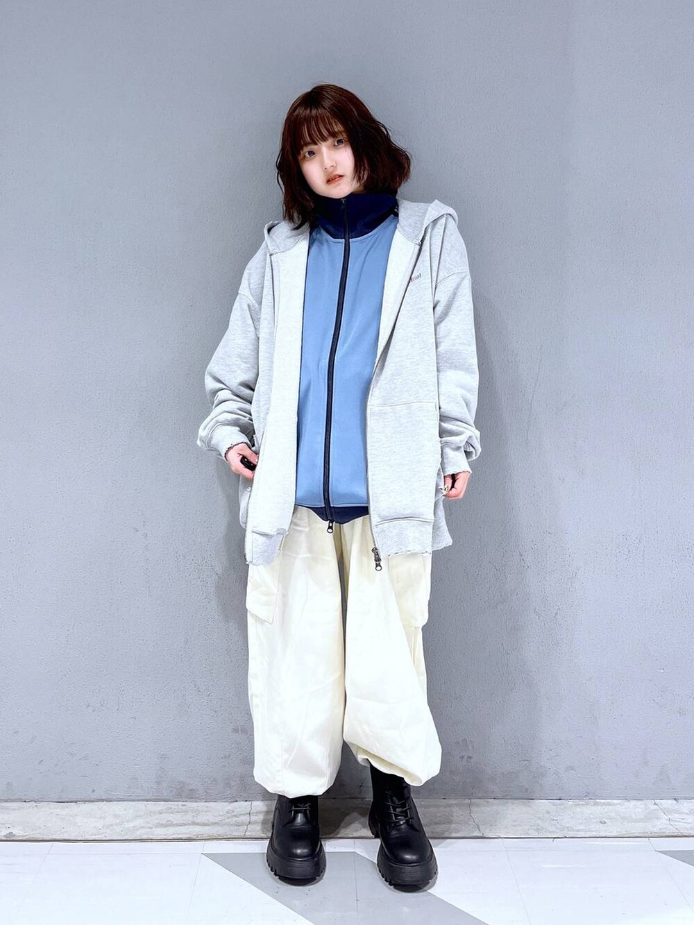 グレー系のパーカー、ブラック系のブーツ、ブルー系のブルゾンを着用したレディースの冬コーディネートの2枚目の写真