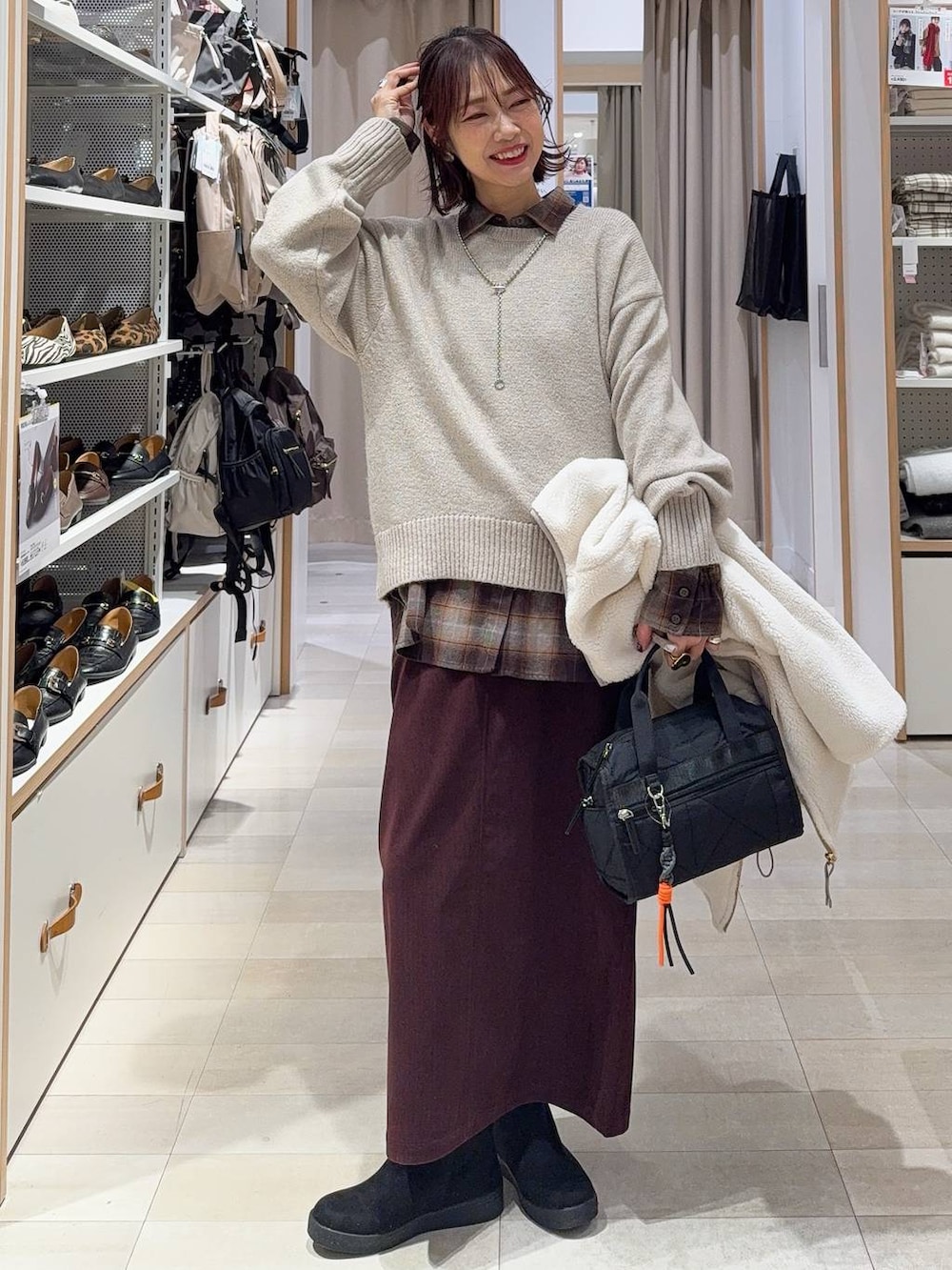 ブラウン系のショルダーバッグ、ブラウン系のチェスターコート、グレー系のワンピースを着用したレディースの冬コーディネートの3枚目の写真