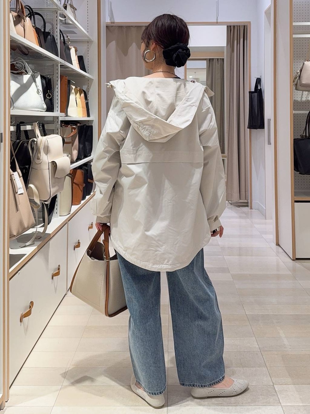 ベージュ系のトートバッグ、ベージュ系のマウンテンパーカー、ブルー系のデニムパンツを着用したレディースの春コーディネートの4枚目の写真