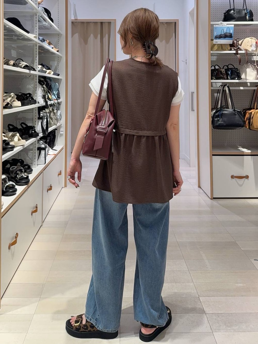 レッド系のボストンバッグ、ブルー系のデニムパンツ、ブラウン系のベストを着用したレディースの夏コーディネートの7枚目の写真