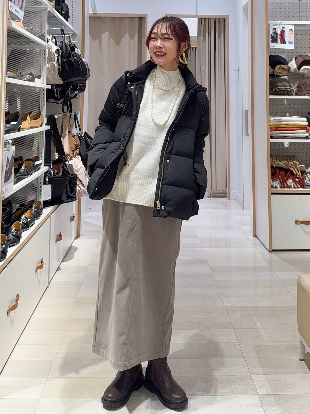 ブラック系のダウンジャケット/コート、ブラウン系のスカート、ホワイト系のニット/セーターを着用したレディースの冬コーディネートの2枚目の写真