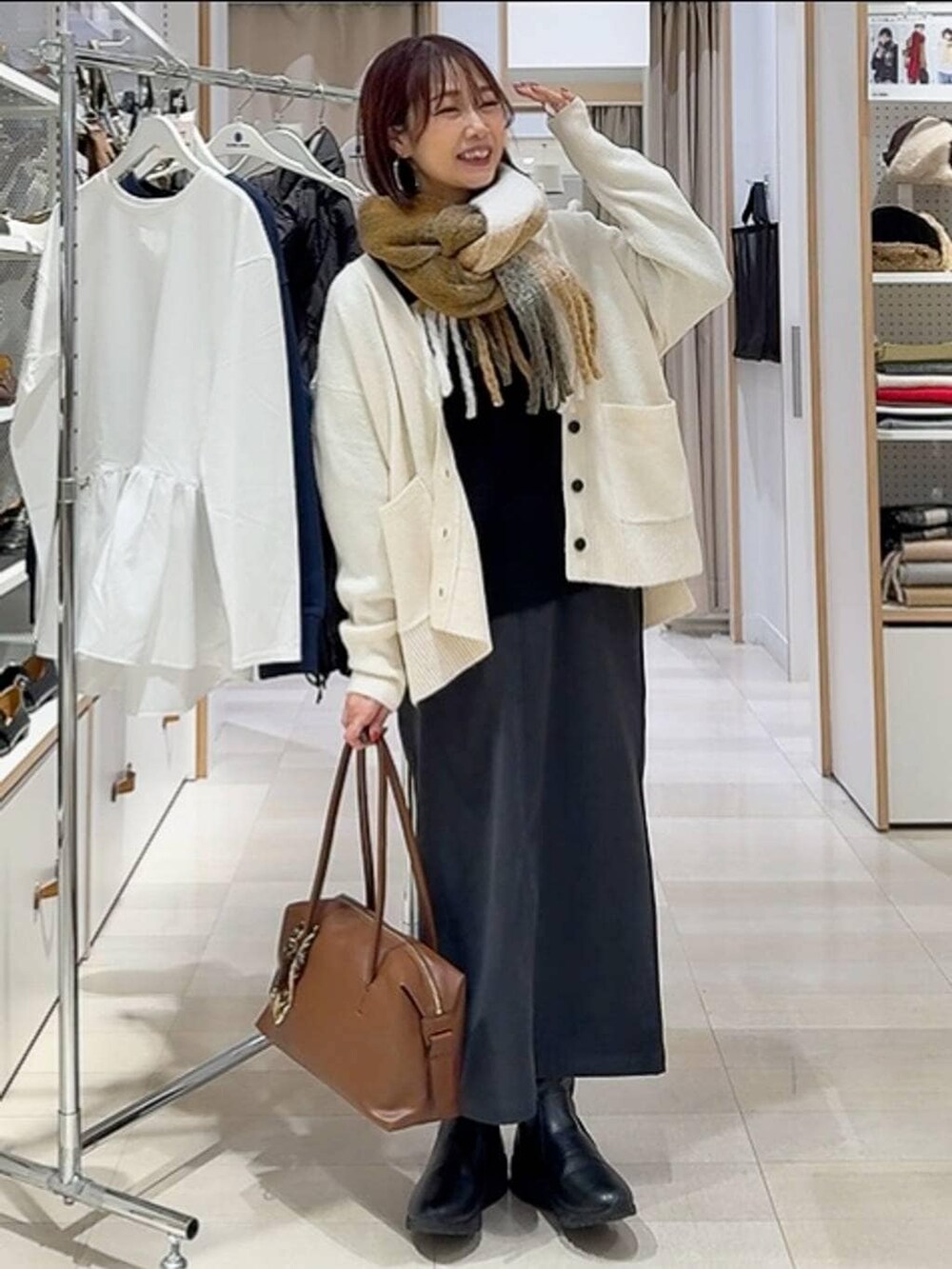 ブラウン系のボストンバッグ、ホワイト系のカーディガン/ボレロ、グレー系のスカートを着用したレディースの秋コーディネートの3枚目の写真