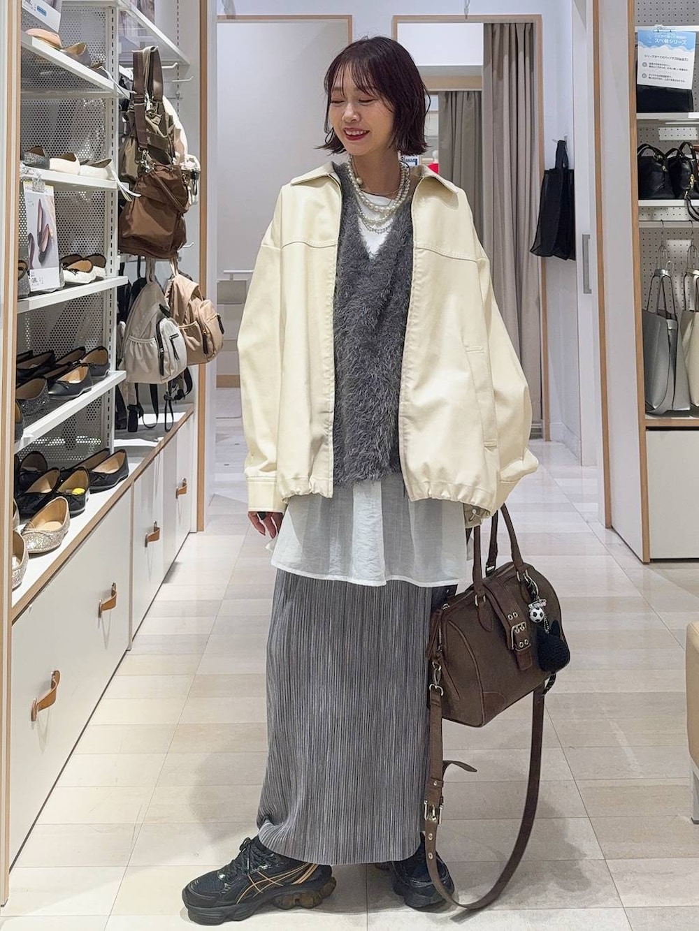 グリーン系のボストンバッグ、ホワイト系のブルゾン、グレー系のスカートを着用したレディースの秋コーディネートの2枚目の写真