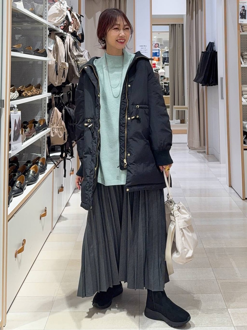 ホワイト系のショルダーバッグ、ブラック系のダウンジャケット/コート、ブラック系のブーツを着用したレディースの冬コーディネートの2枚目の写真