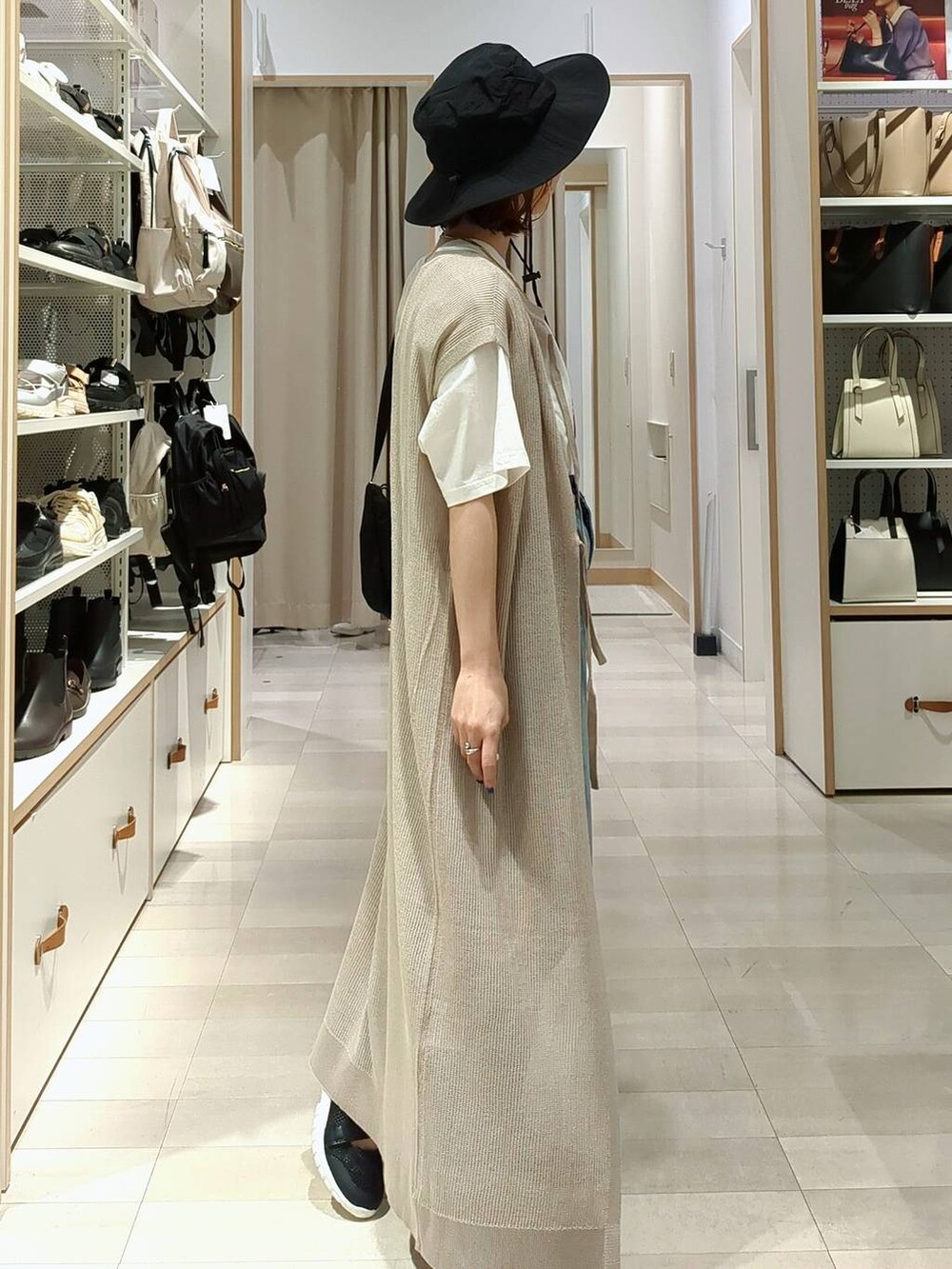 ブラック系のスニーカー、ブルー系のデニムパンツ、ベージュ系のワンピースを着用したレディースの春コーディネートの5枚目の写真