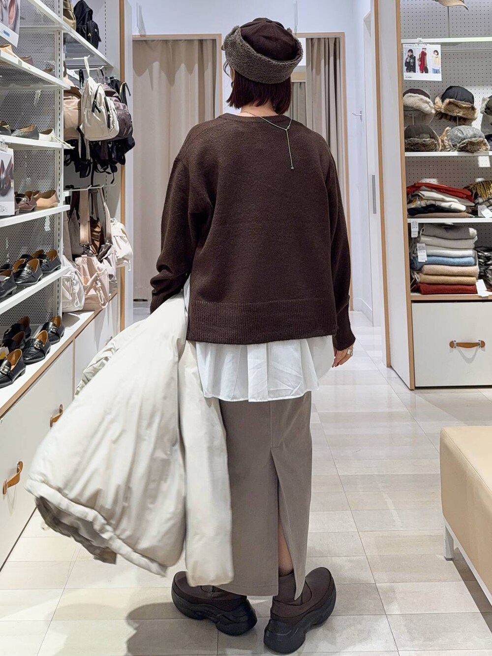 ブラック系のショルダーバッグ、ベージュ系のダウンジャケット/コート、ブラウン系のスカートを着用したレディースの秋コーディネートの6枚目の写真