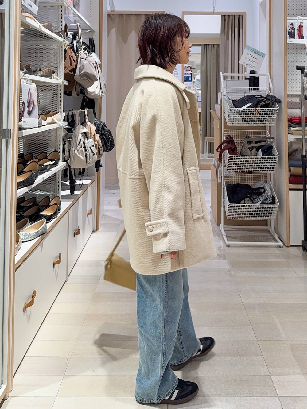 ブルー系のデニムパンツ、イエロー系のショルダーバッグ、ホワイト系のステンカラーコートを着用したレディースの冬コーディネートの5枚目の写真