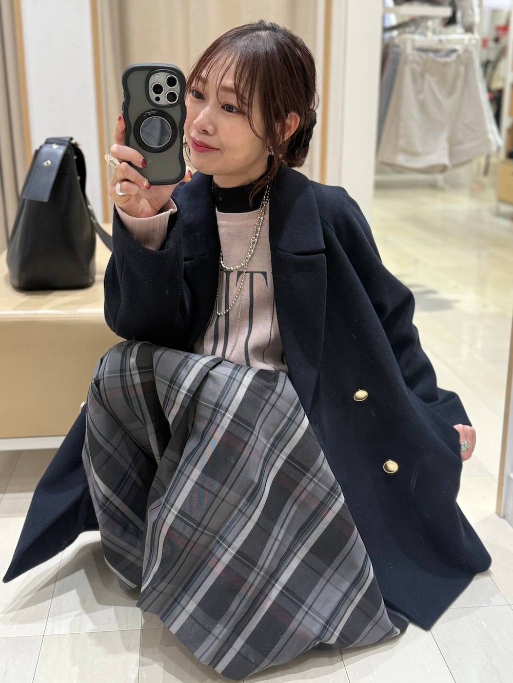 ブラック系のショルダーバッグ、ブルー系のチェスターコート、グレー系のスカートを着用したレディースの冬コーディネートの2枚目の写真