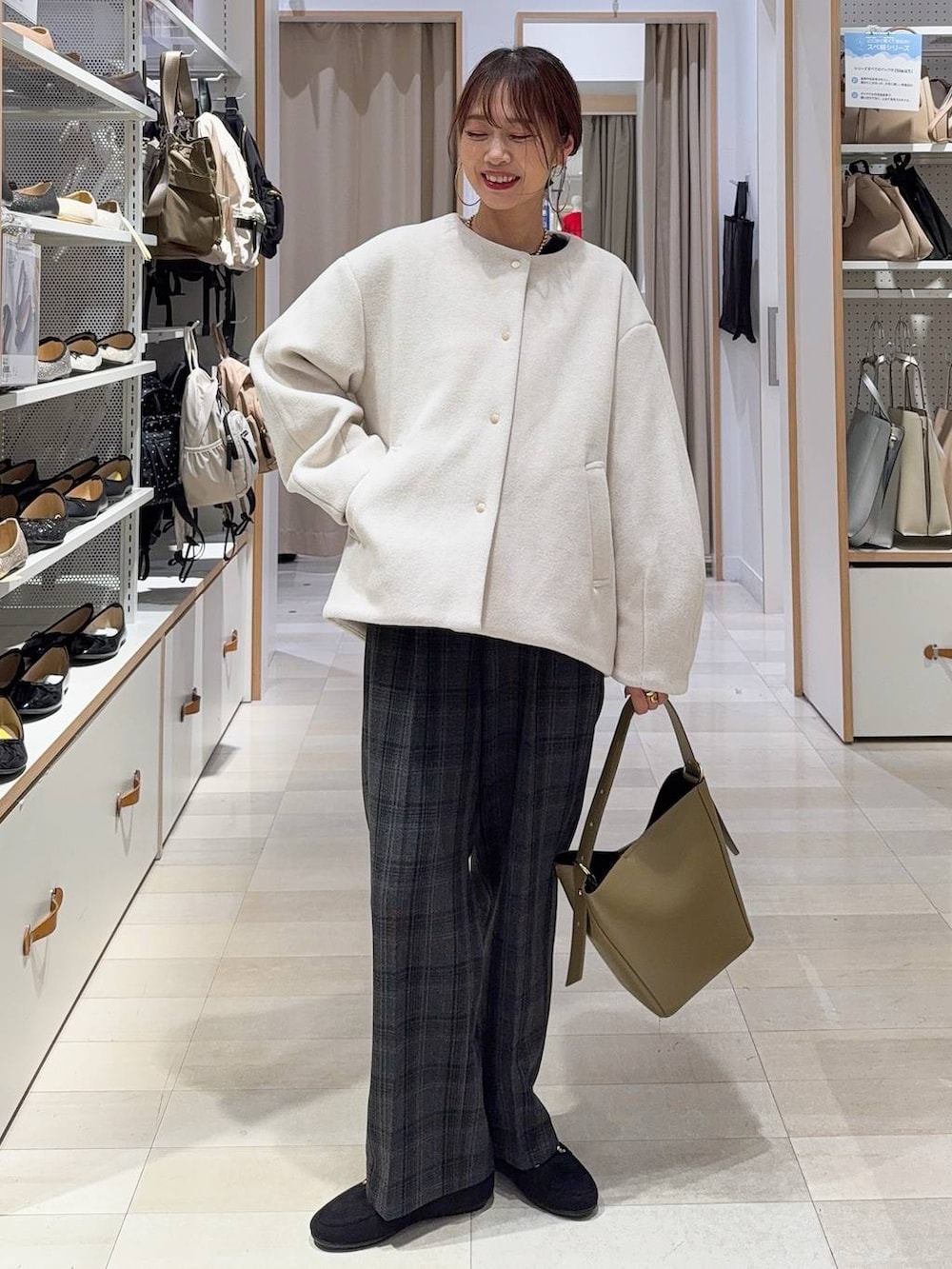 グリーン系のショルダーバッグ、ベージュ系のノーカラーコート、ブラック系のニット/セーターを着用したレディースの秋コーディネートの2枚目の写真