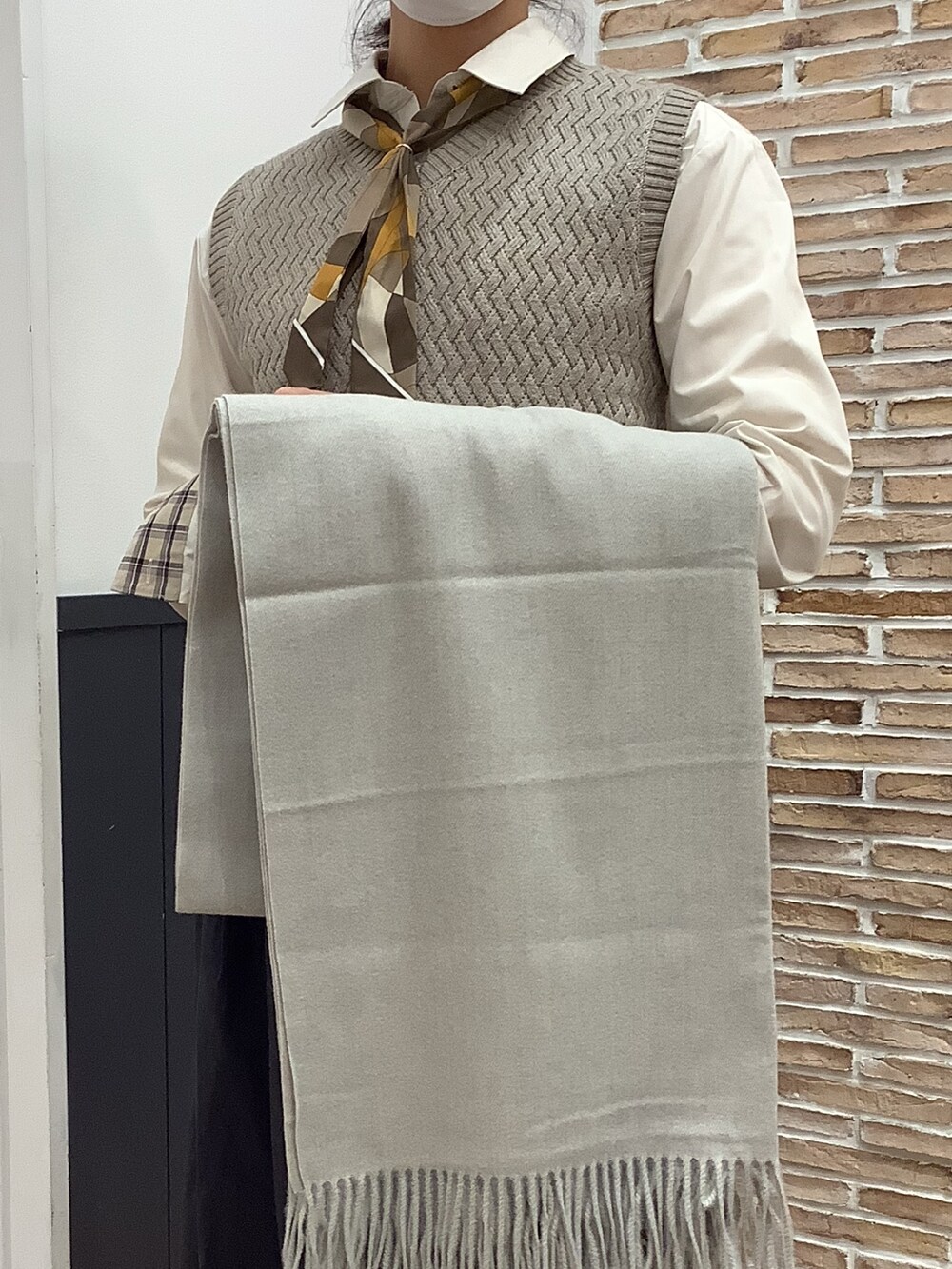 ベージュ系のビジネスシャツ、ベージュ系のニット/セーター、グレー系のストール/ショールを着用したレディースの冬コーディネートの2枚目の写真