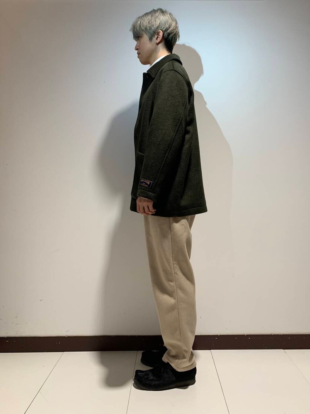 ホワイト系のTシャツ/カットソー、ベージュ系のその他パンツ、グリーン系のステンカラーコートを着用したメンズの冬コーディネートの5枚目の写真