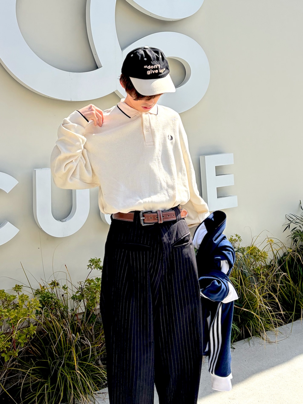 ホワイト系のニット/セーター、ブラック系のスラックス、ブルー系のジャージを着用したメンズの春コーディネートの2枚目の写真