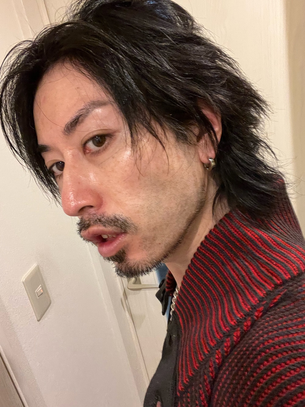 ブラック系のブーツ、グレー系のスラックス、レッド系のカーディガン/ボレロを着用したメンズの冬コーディネートの3枚目の写真