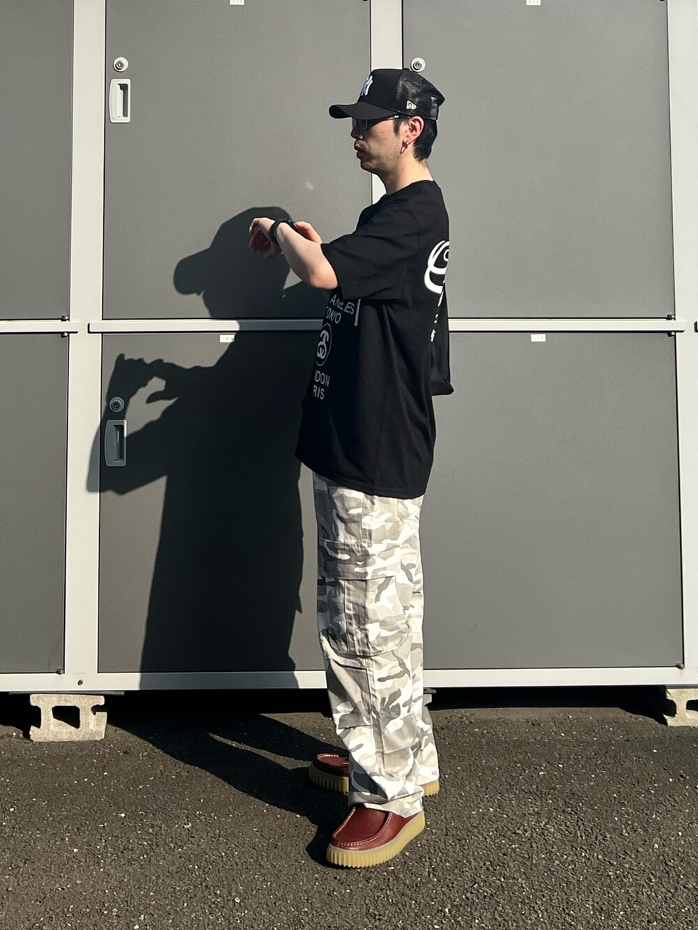 ブラック系のTシャツ/カットソー、ブラック系のトートバッグ、ブラウン系のモカシン/デッキシューズを着用したメンズの夏コーディネートの3枚目の写真