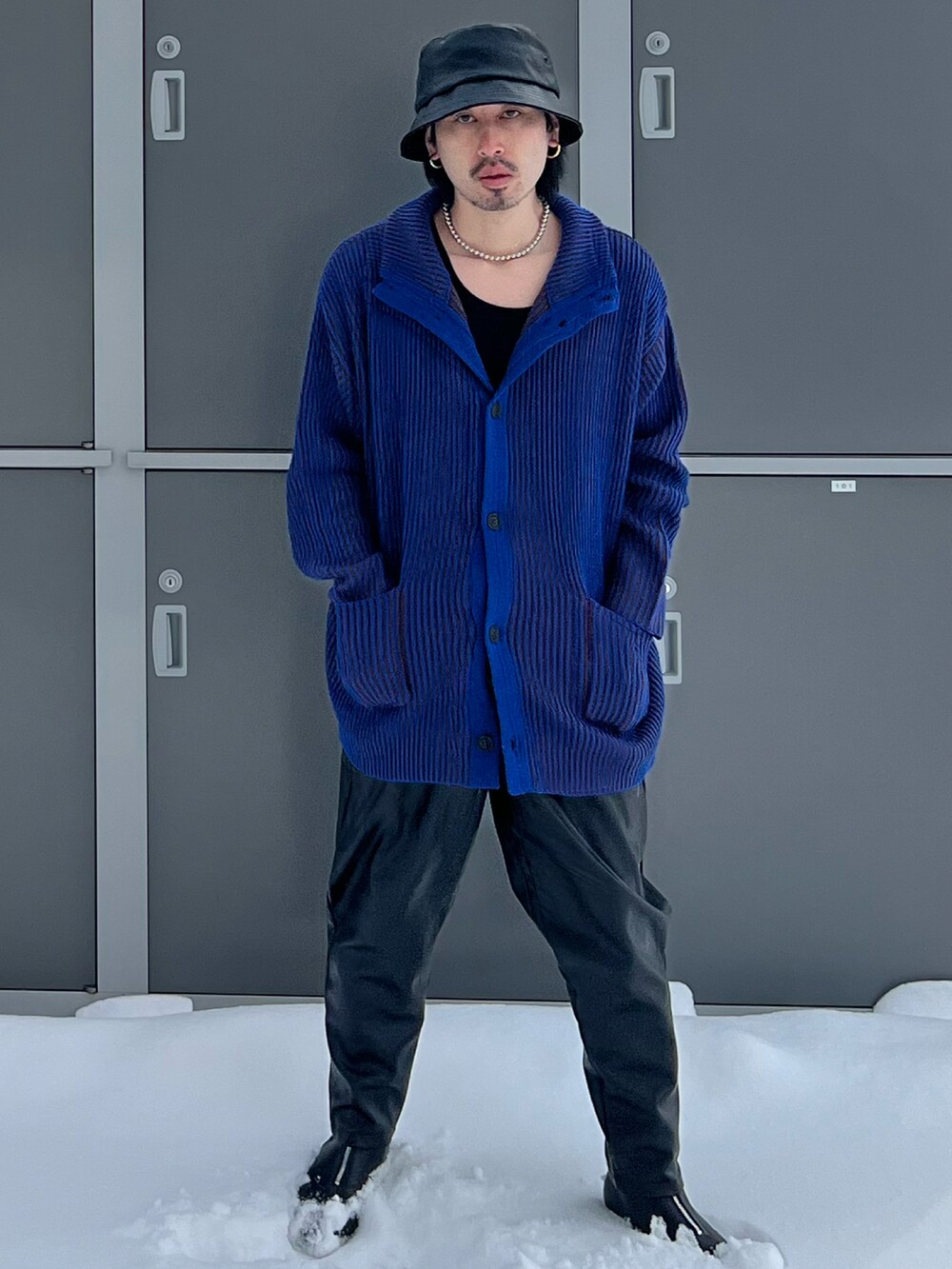 ブラック系のスラックス、ブルー系のカーディガン/ボレロ、ベージュ系のタンクトップを着用したメンズの冬コーディネートの2枚目の写真