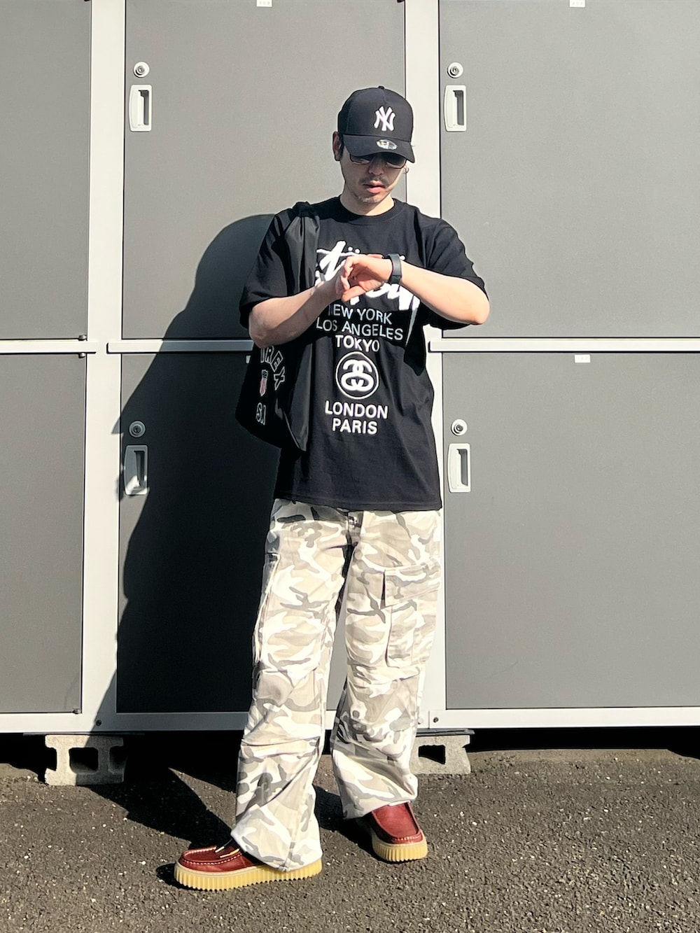 ブラック系のTシャツ/カットソー、ブラック系のトートバッグ、ブラウン系のモカシン/デッキシューズを着用したメンズの夏コーディネートの2枚目の写真