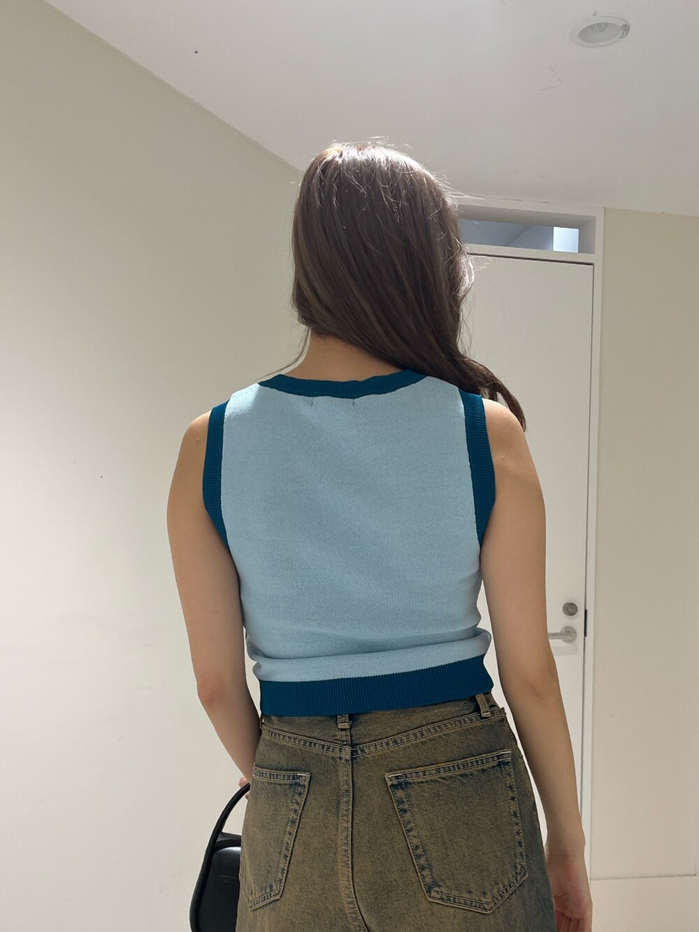 ブラック系のハンドバッグ、ブルー系のデニムパンツ、ブルー系のニット/セーターを着用したレディースの夏コーディネートの6枚目の写真